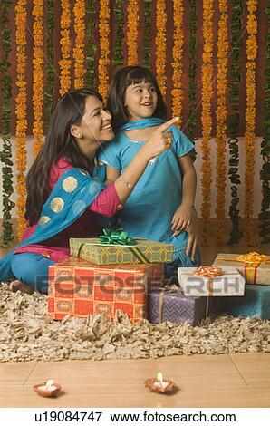 Stock Photo - Young woman and her daughter sitting behind diwali gifts. Fotosearch