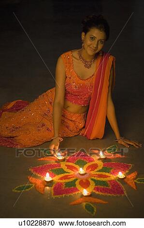 Stock Image - Young woman decorating rangoli with oil lamps. Fotosearch