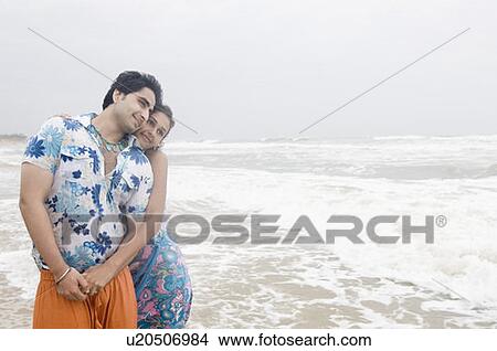 Young woman embracing a young man from behind on the beach View Large Photo Image Picture - Young woman embracing a young man from behind on the beach. Fotosearch