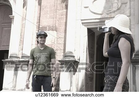 Stock Photo - Young woman filming on a young man with a home video camera, Goa, India. Fotosearch