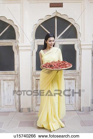 Stock Photograph - Young woman holding a tray of red chili peppers and smiling. Fotosearch