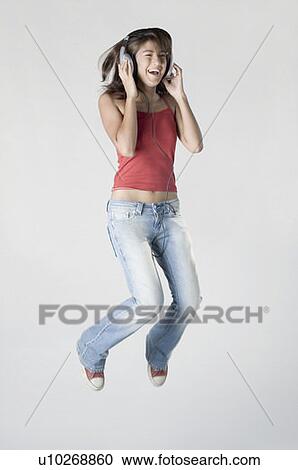 Stock Image - Young woman listening to music and jumping. Fotosearch