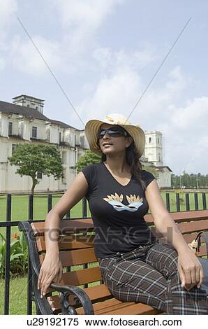 Stock Photography - Young woman sitting on a bench with a cathedral in the background, Se Cathedral, Goa, India. Fotosearch