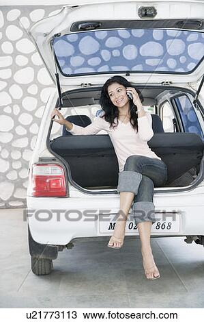 Young woman sitting on the boot of a car and talking on a mobile phone View Large Photo Image Stock Image - Young woman sitting on the boot of a car and talking on a mobile phone. Fotosearch