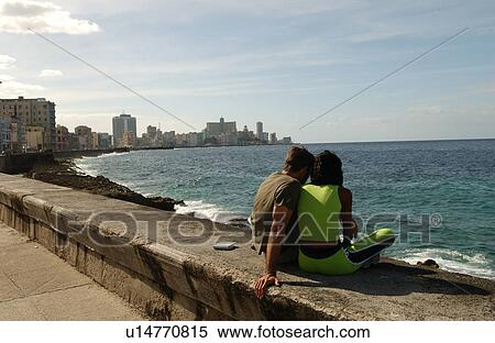 Stock Photography - Rear view of a couple sitting together on a wall facing the sea. Fotosearch