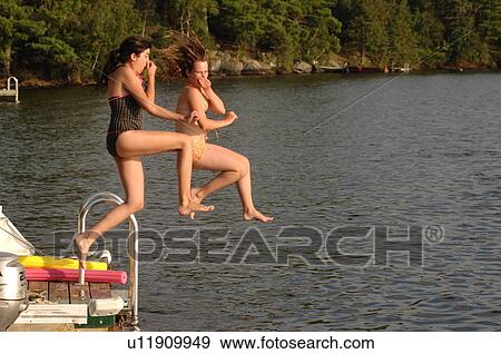 Stock Photo - Two teenage girls jumping into the lake. Fotosearch