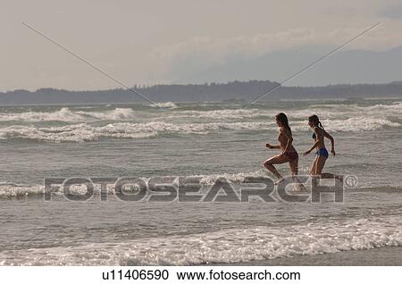 Stock Image - Two women running into ocean. Fotosearch