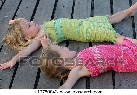 Stock Image - Two young girl's lying on a wooden deck. Fotosearch