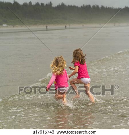 Stock Image - Two young girls running in water. Fotosearch