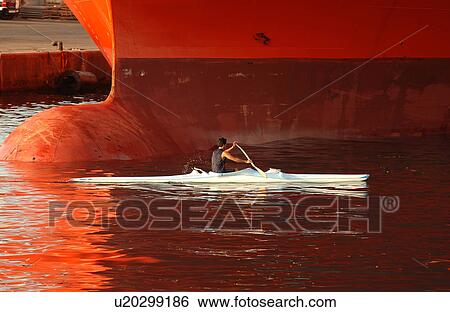 A man rowing a canoe near a large ship View Large Photo Image Stock Photograph - A man rowing a canoe near a large ship. Fotosearch