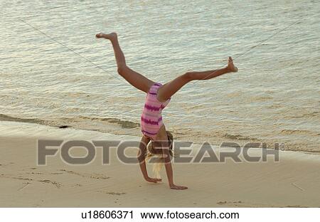 Stock Image - A young girl doing cartwheels on a beach. Fotosearch