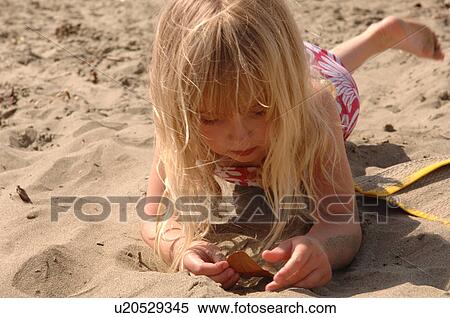 Stock Photography - Young girl playing in sand on beach. Fotosearch