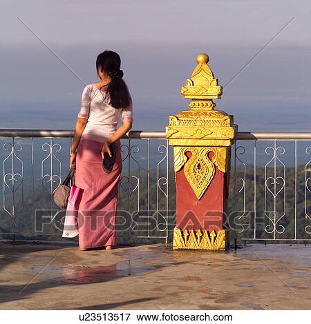 Stock Photo - Burmese woman standing at railing at Gold Rock shrine. Fotosearch