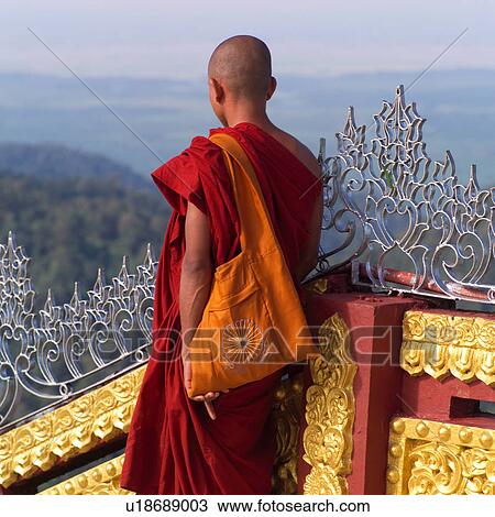 Stock Image - Monk standing at banister of staircase at Golden Rock. Fotosearch