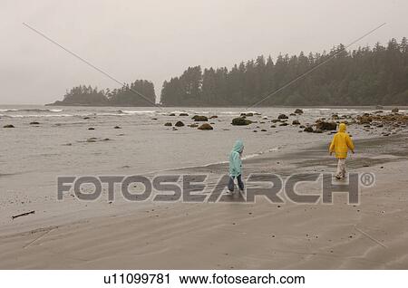 Stock Image - People walking on beach on a cloudy day. Fotosearch