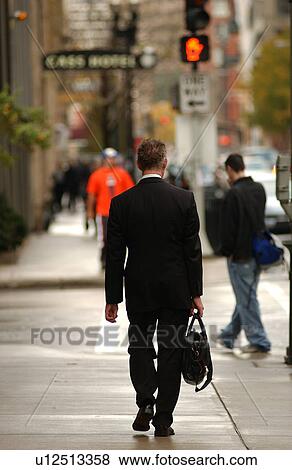Stock Photo - View of a businessman walking on a sidewalk carrying a briefcase. Fotosearch