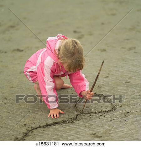 Stock Image - Child writing in the sand on beach. Fotosearch