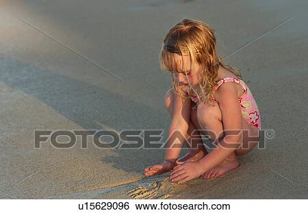Stock Photograph - Close-up of a young girl playing with sand on a beach. Fotosearch