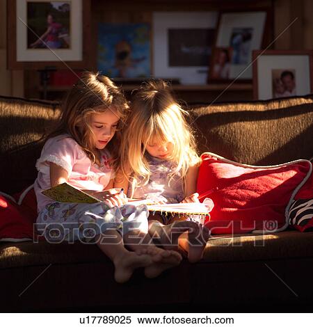 Stock Photography - Two girls on a sofa looking at books. Fotosearch