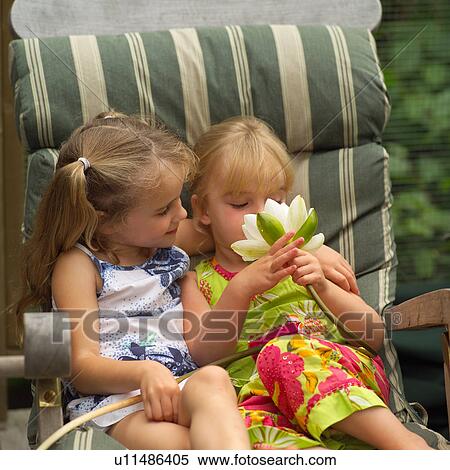 Stock Photography - Two young girls sitting in a chair holding a lotus. Fotosearch