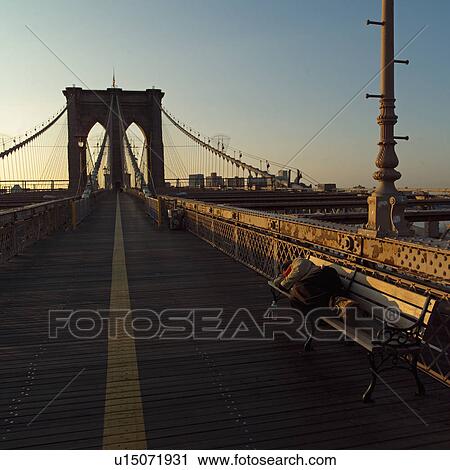 Stock Image - Person lying on a bench on the Brooklyn Bridge, New York City. Fotosearch