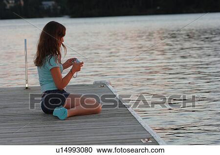 Stock Image - Teenage girl sitting on a dock. Fotosearch