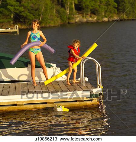 Stock Image - Two young girls standing on a pier in swimsuits at Lake of the woods, Ontario, Canada. Fotosearch