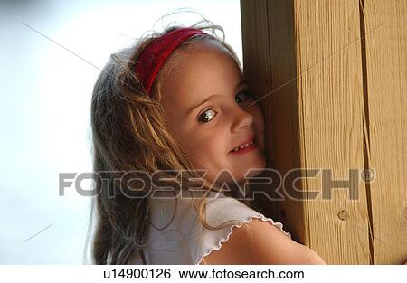 Stock Photograph - Young girl hugging a wooden post smiling. Fotosearch
