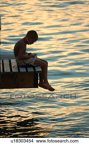 Picture - A young man sitting on a pier. Fotosearch