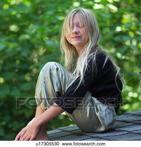 Stock Image - Side profile of a young girl sitting in a garden. Fotosearch
