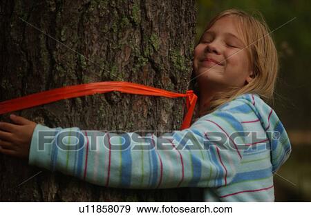 Stock Photo - Young girl hugging a tree with a red ribbon around it. Fotosearch