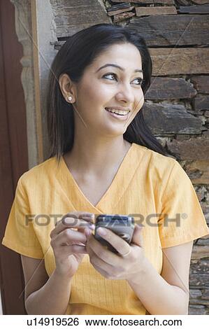 Stock Photograph - Close-up of a young woman holding a mobile phone and smiling. Fotosearch