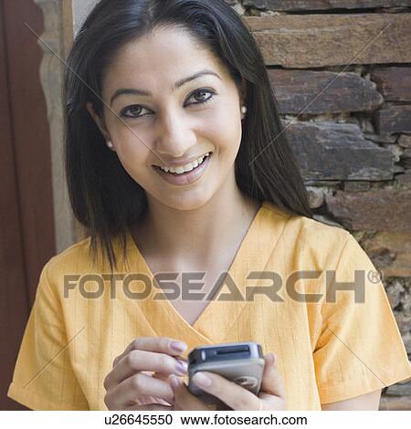 Stock Image - Portrait of a young woman holding a mobile phone and smiling. Fotosearch