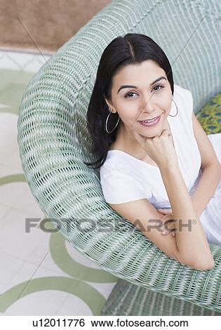 Stock Photograph - Portrait of a young woman sitting on a couch with her hand on her chin. Fotosearch