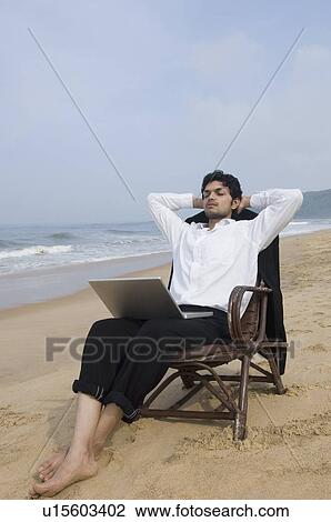 Stock Image - Businessman sitting in an armchair with a laptop on the beach. Fotosearch