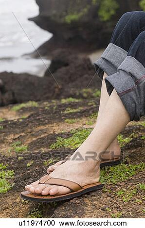 Stock Image - Low section view of a person's legs wearing flip-flops. Fotosearch