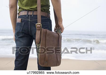 Mid section view of a young man carrying a shoulder bag on the beach View Large Photo Image Stock Photography - Mid section view of a young man carrying a shoulder bag on the beach. Fotosearch