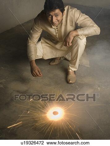 Stock Image - Portrait of a mid adult man crouching near a firecracker and smiling. Fotosearch
