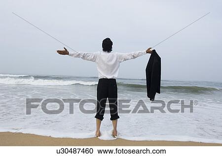 Stock Image - Rear view of a young man standing on the beach. Fotosearch