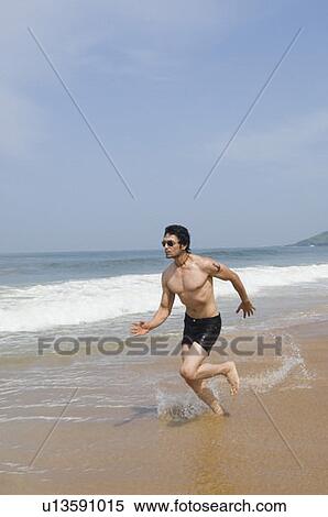 Stock Photography - Side profile of a young man running on the beach. Fotosearch