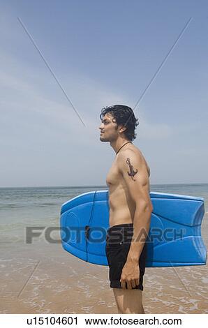 Side profile of a young man standing on the beach with a surfboard View Large Photo Image Stock Image - Side profile of a young man standing on the beach with a surfboard. Fotosearch