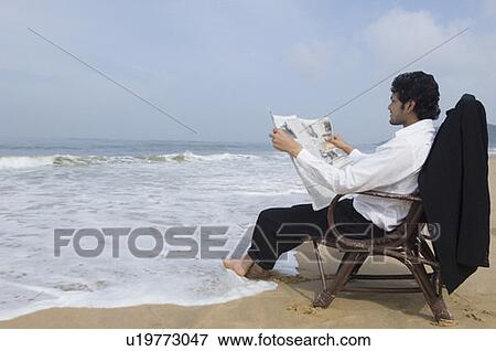 Young man reading a newspaper on the beach View Large Photo Image Stock Photo - Young man reading a newspaper on the beach. Fotosearch