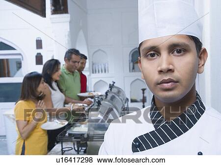 Stock Photo - Portrait of a chef with two mid adult couples having food behind him. Fotosearch
