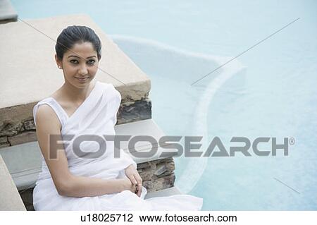 Stock Image - Portrait of a young woman sitting on the steps of a swimming pool. Fotosearch