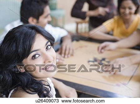 Portrait of a young woman smiling with her friends playing carom beside her View Large Photo Image Stock Image - Portrait of a young woman smiling with her friends playing carom beside her. Fotosearch