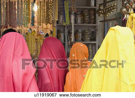 Stock Photo - Rear view of four women standing at a market stall. Fotosearch