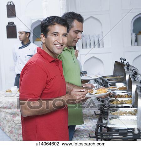 Two mid adult men having food in a party with a chef standing in the background View Large Photo Image Stock Image - Two mid adult men having food in a party with a chef standing in the background. Fotosearch