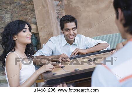 Stock Photograph - Two young men and a young woman playing carom. Fotosearch