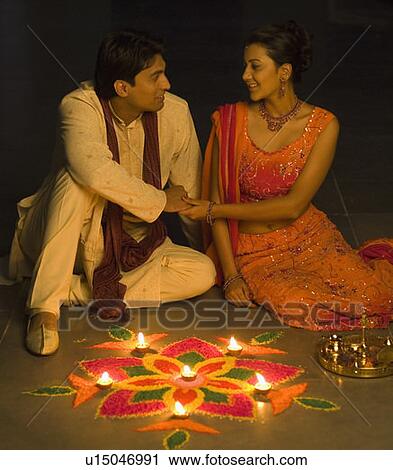 Stock Image - Young couple sitting behind a rangoli. Fotosearch