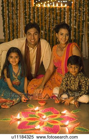 Stock Photography - Young couple sitting with their children in front of rangoli. Fotosearch